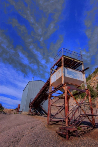 Mining structure or water tower on stilts against a vivid blue sky, appearing to be in a desert or arid location.