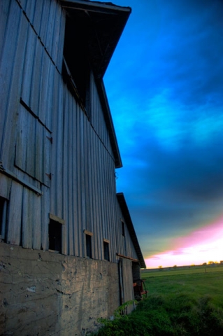 Side view of a weathered barn or wooden structure against a dramatic blue sky at dusk or dawn.