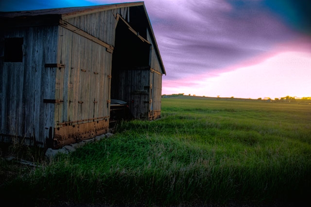 Side view of a weathered barn or wooden structure at dusk with purple sky gradient.