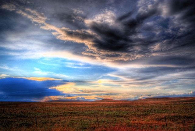 Dramatic landscape with cloudy sky over what appears to be fields or plains with blue mountains in the distance.