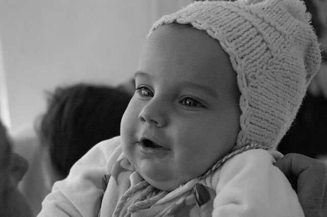 A close-up of a baby wearing a light-colored bonnet or cap, in black and white.