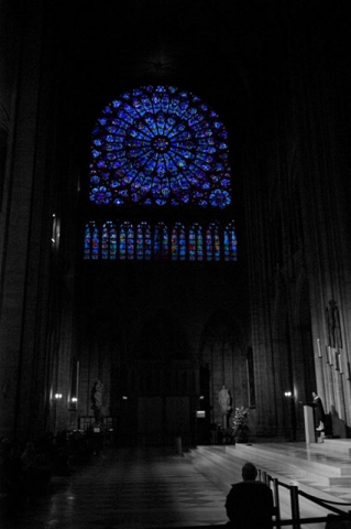 The interior of what appears to be a cathedral or church with a prominent stained glass rose window illuminated in blue against a dark background.