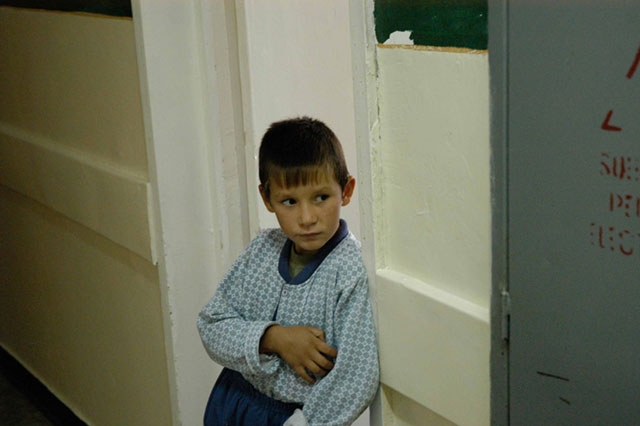A young child in light blue clothing standing against a wall or near a doorway.
