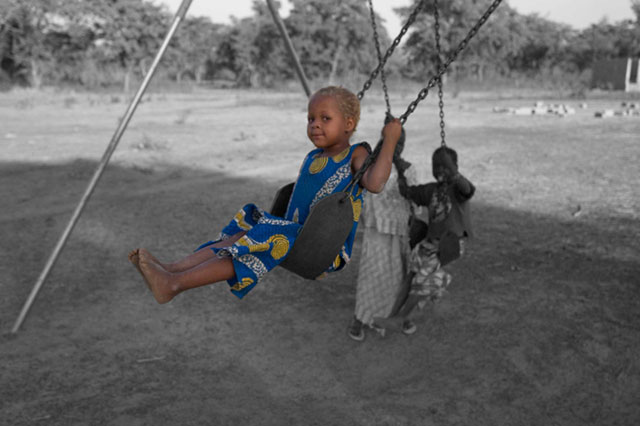 A small child sitting in what appears to be an outdoor swing or similar equipment in a black and white image.