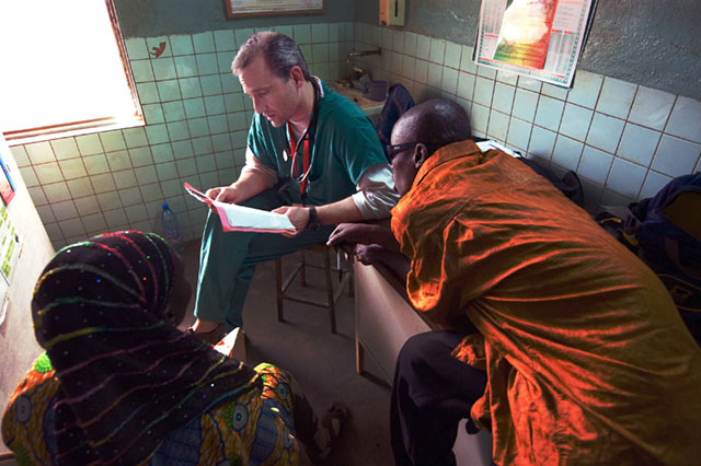 People in what appears to be a medical or care setting, where someone in green clothing seems to be attending to others.