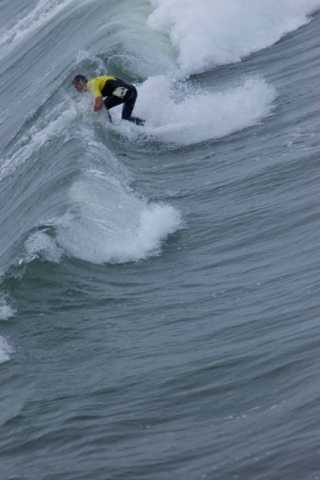 A closer view of a surfer riding a large wave, with white spray surrounding them.
