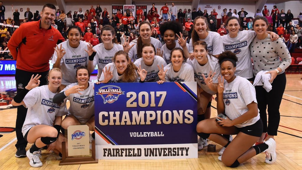 a volleyball team posing with a championship banner and trophy