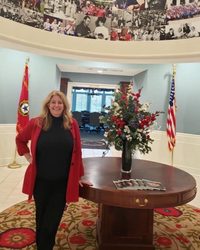 Kelly Circle alongside circular table with flower and pamphlets in front of doors opened to reveal conference table