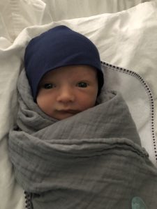 Caroline Kastor newborn baby, Robert "Bobby", swaddled in a grey blanket wearing a dark blue hat
