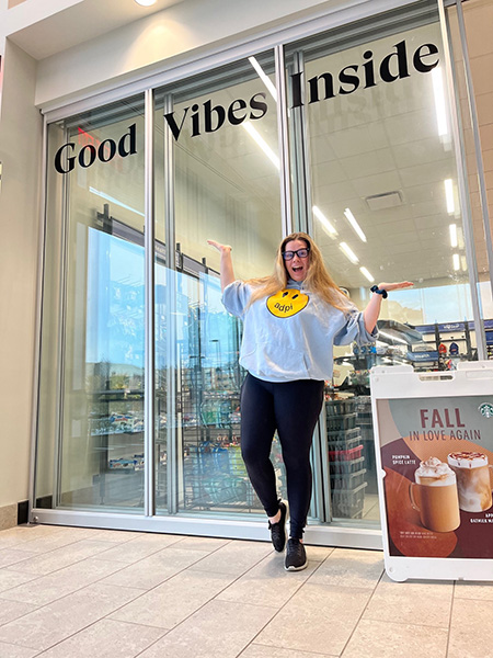 A woman smile and poses in front of a window with the words 'Good Vides Inside' on it