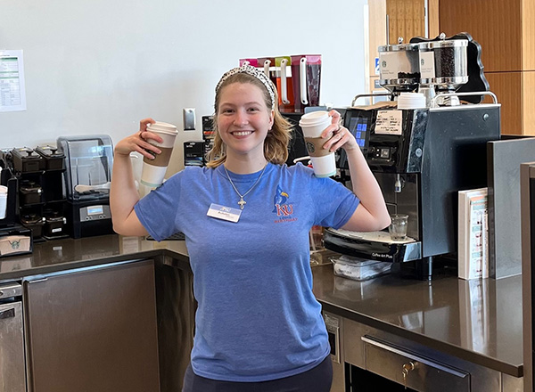 A barista smiles holding up two cups of coffee