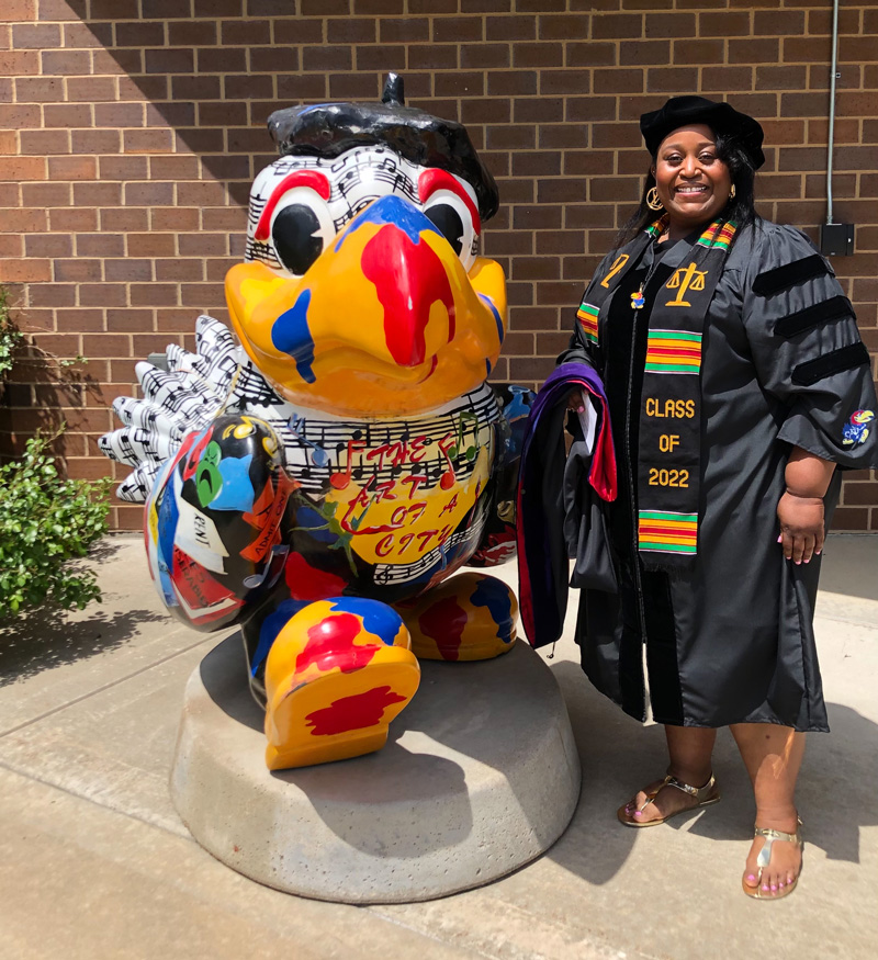 Lakisha Cooper poses in graduation regalia with a Jayhawk statue outside the Lied Center of Kansas