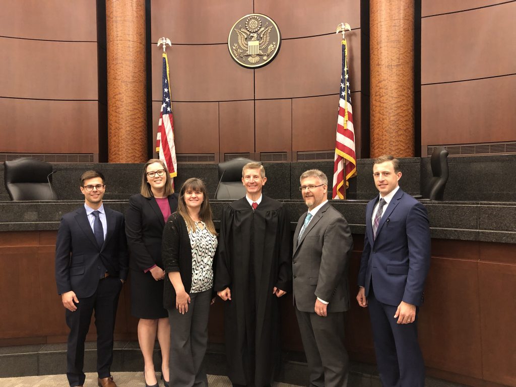 Michael Hayes standing with a group of six people all dressed formally standing in a courtroom.