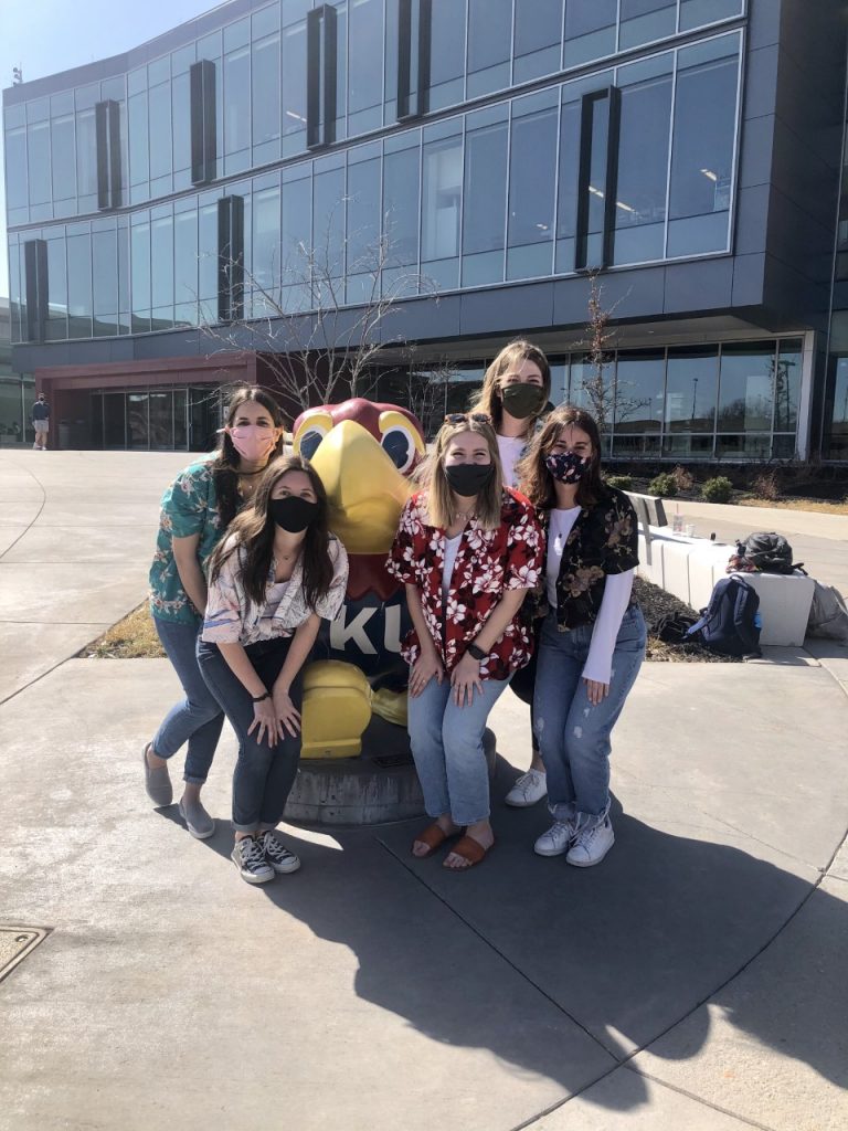 Group of five law students standing next to a Jayhawk statue outside Burge Union while wearing vacation-themed attire.