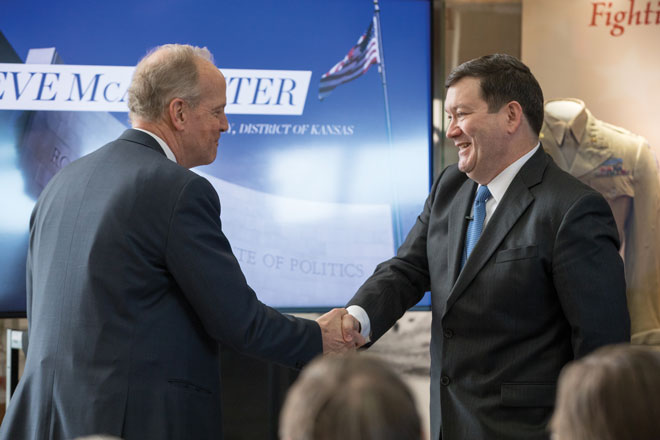 Two men in suits shaking hands at a political event