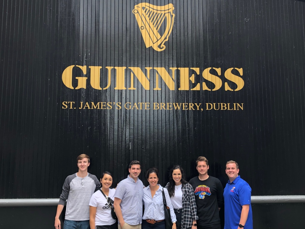 A group of people posing for a photo next to the Guinness brewery board in Dublin, Ireland
