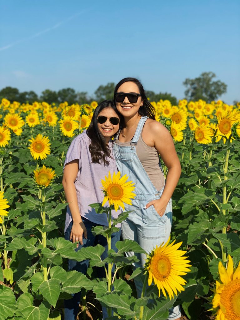 Valeria Carbajal and Marisol Garcia pose for a photo in a field of sunflowers