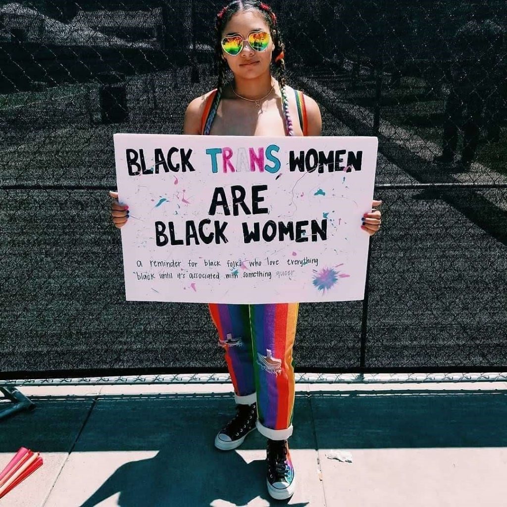 Bria Nelson outside holding a sign that says 'black trans women are black women, a reminder for black folks who love everything black until it's associated with something queer.