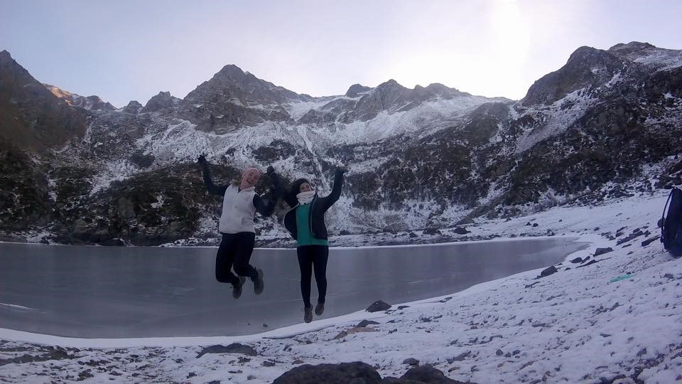 Miranda and Camila jump alongside a snowy, mountainous lake.
