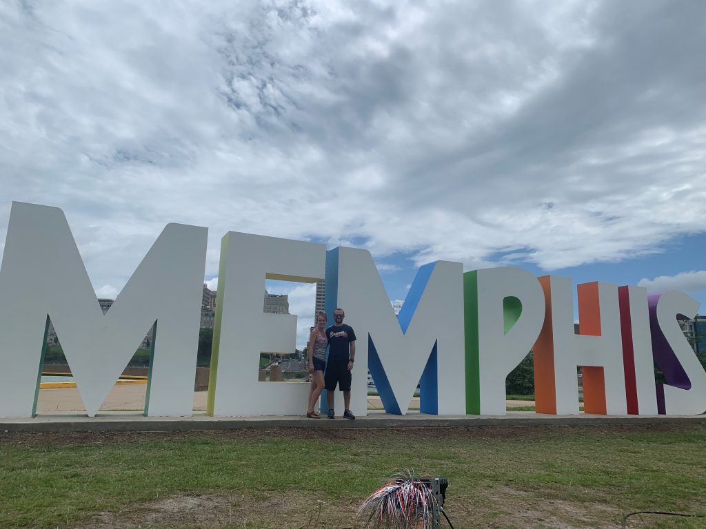 Two people stand in front of a tall sculpture of the word Memphis