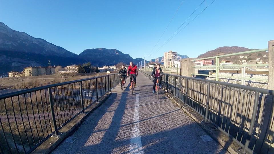 Three students on bike trail in front of buildings and mountains.