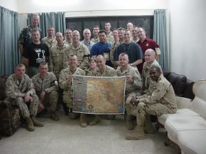 Eric McMillin with a mixed group in Army fatigues and plain clothes holding up a map