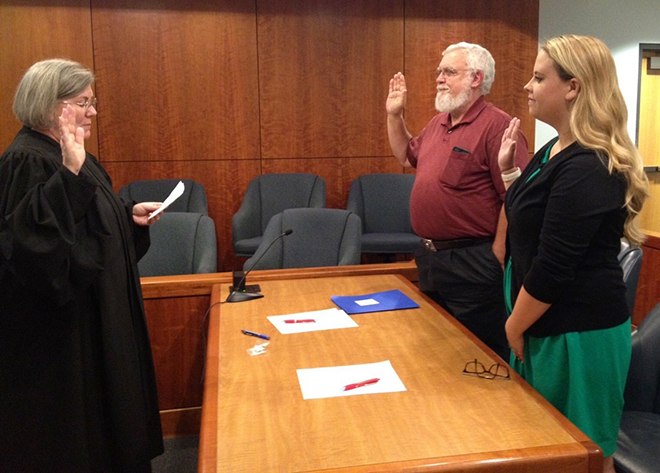 Katie Gilman holding her right hand up standing next to one other person in front of a judge