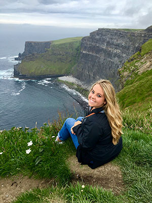 Katie Gilman sitting on a cliff with an ocean view Ireland.