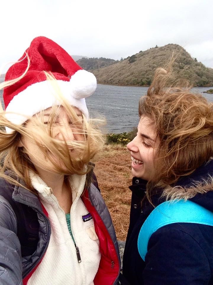 Miranda and Gili laughing with hair blowing in front of water and mountains.