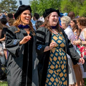 Lindsay Strong and Carly Masenthin walking with their graduation cap and gown.