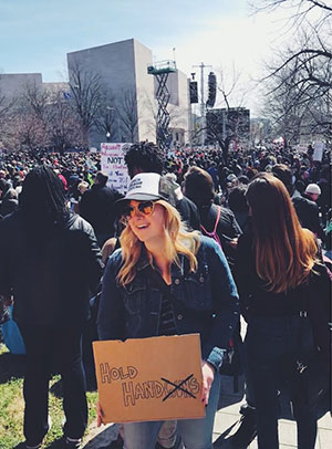 Maslyn Locke holds handmade cardboard sign against guns at outdoor gathering/protest