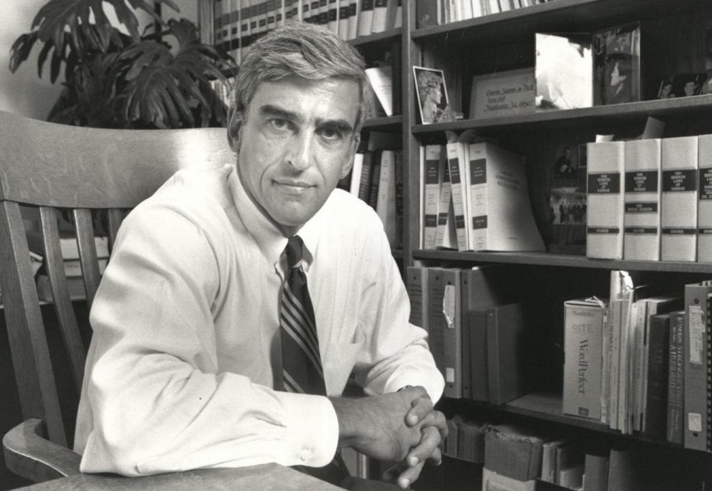John Peck in wooden chair in front of bookshelves