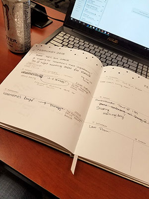 law student planner, lap top, and energy drink laid out on wooden desk