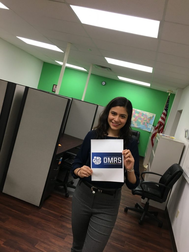 Samantha Natera in office space holding up paper with DMRS logo