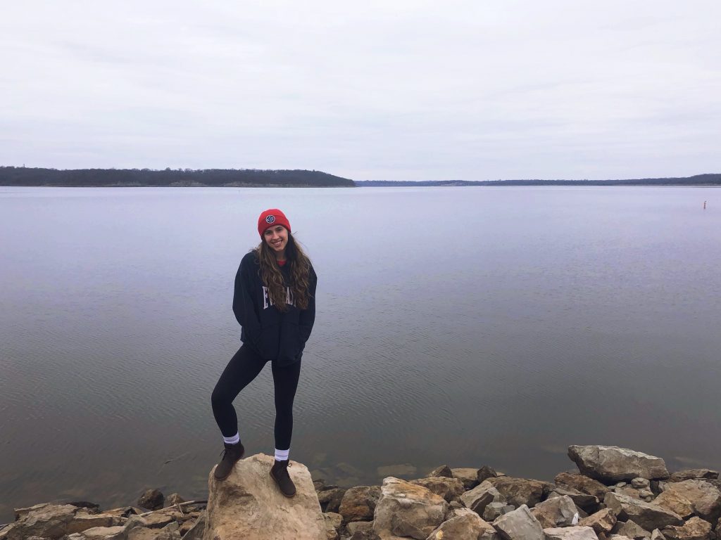 A woman stands on a rock in front of a lake